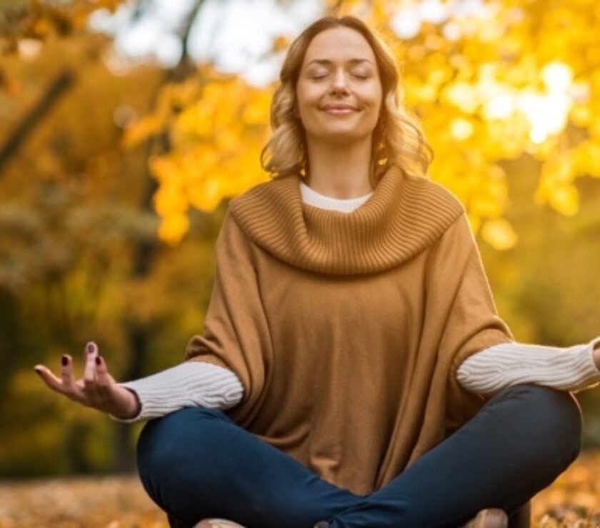 Smiling woman meditating in autumn day at the park.